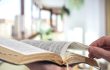 A man holds a Bible and reads a book on the terrace. Morning time.